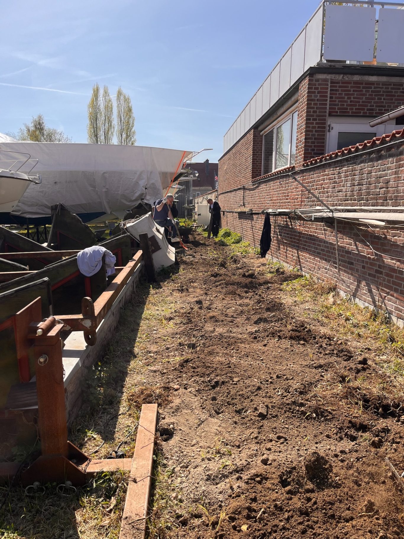 Blick auf einen unebenen Gartenbereich mit Erde und Bauarbeiten an einer Wand.