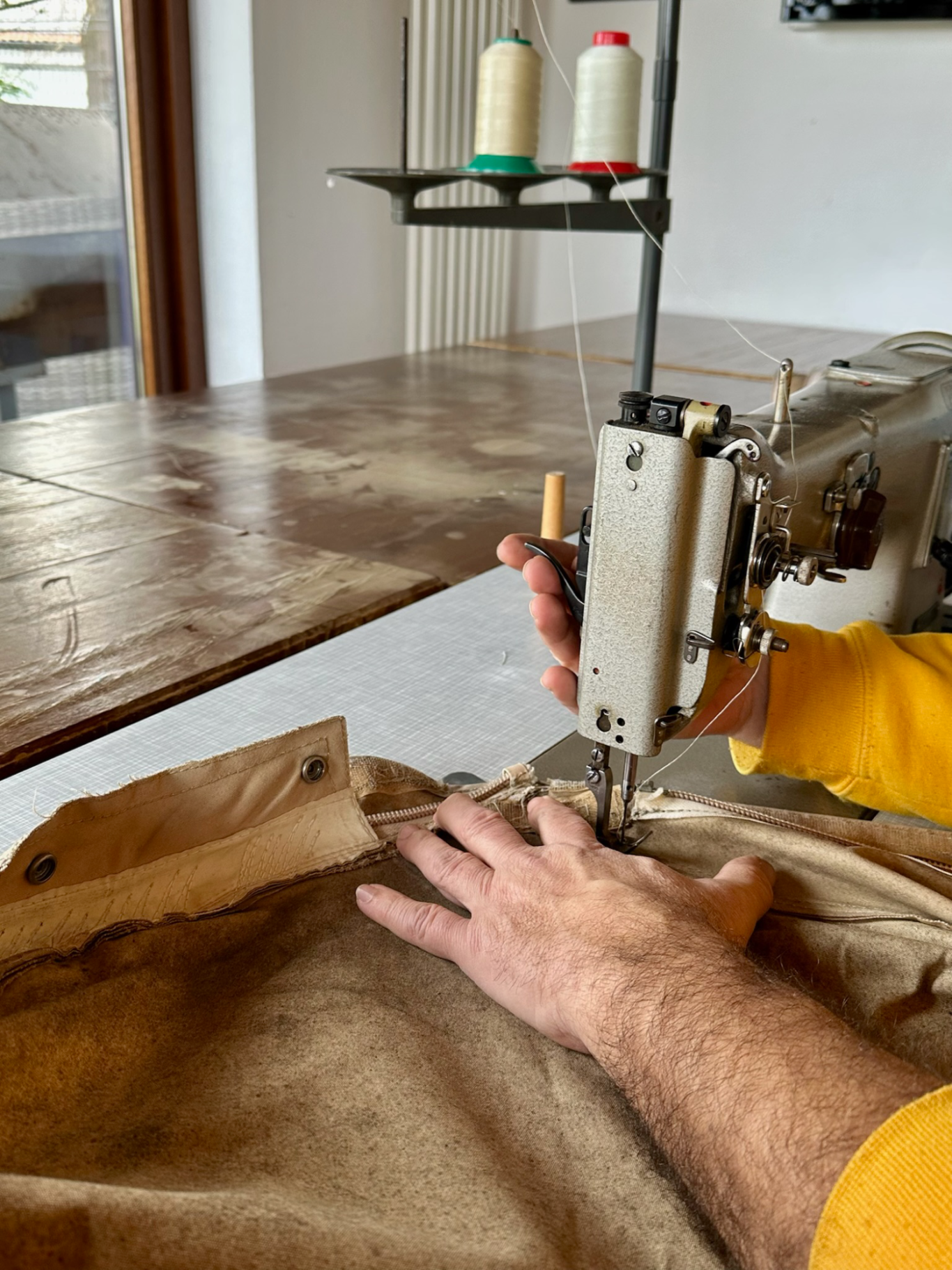 Eine Hand bedient eine Nähmaschine, während Stoff zum Nähen geführt wird.