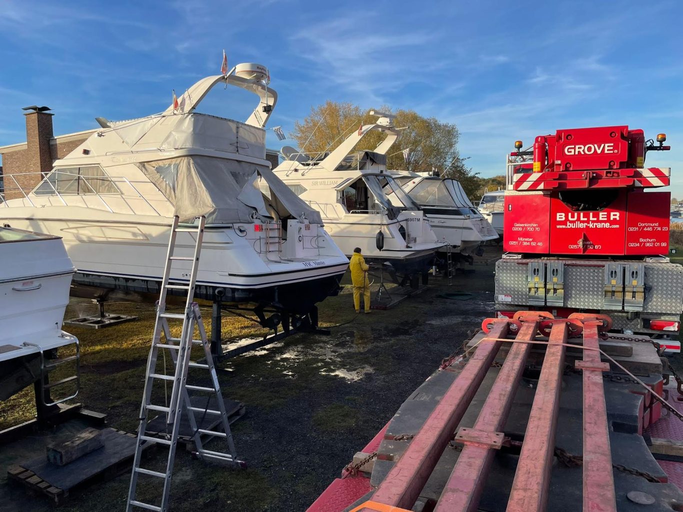 Drei weiße Boote in einer Werft, daneben ein rotes Fahrzeug und eine Leiter.