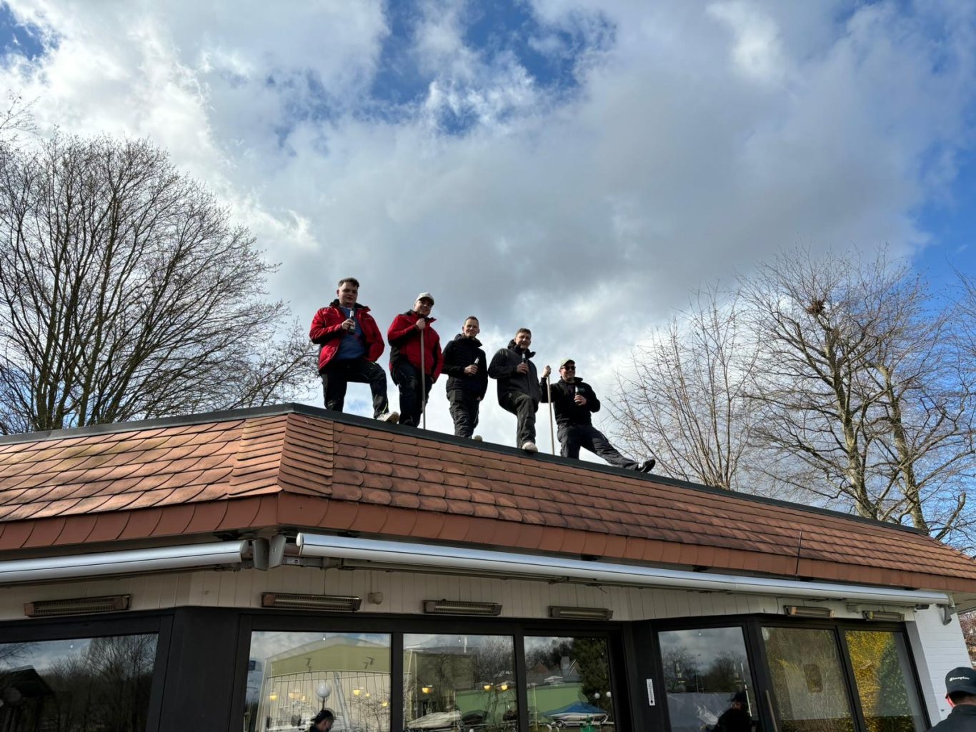Fünf Personen stehen auf dem Dach eines Hauses unter einem bewölkten Himmel.